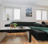 Living room in a two-room apartment with a sofa, table, and wooden decor flooring.
