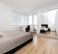 Bright bedroom in a 2-room apartment with wood-patterned flooring, a bed, and a wardrobe.
