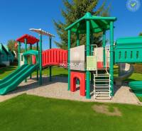 A cottage in Liptovský Mikuláš with a lawn, terrace, and children's playground, under a blue sky.
