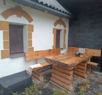 A cottage in Píla with wooden seating on a stone terrace and decorated windows.