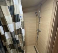 A shower corner in a cabin with tiles and a curtain in a striped design.