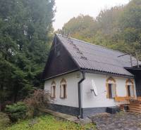 A cottage in the village of Píla surrounded by forest and a stone path.