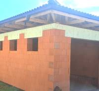 A family house under construction in Hokovce with unplastered brick walls and a wooden roof structure.