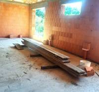 Construction of a family house in Hokovce with raw brick walls and wooden boards on the ground.