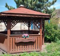 A wooden gazebo surrounded by greenery and a fence on Štúrova Street near a family house.