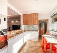 A kitchen in a family house with a sink, refrigerator, oven, table, and orange chairs.