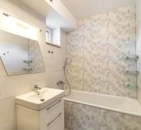 A bathroom in a family house with a rectangular bathtub and an asymmetrical mirror on the wall.