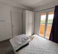 Bedroom with a wardrobe, bed, and view from a 3-room apartment with a wooden decor floor.