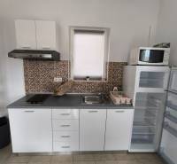 A kitchen in a 3-room apartment with a cooktop, sink, and a free-standing refrigerator.