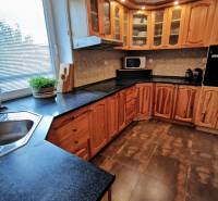 A kitchen in a family house with wooden cabinets, a dark countertop, and tiles.