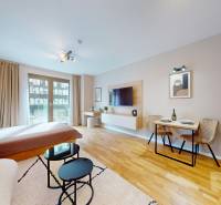 A one-room apartment with a wooden decor floor, a bed, a dining table, and a TV.