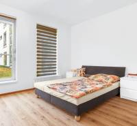 Bedroom in a 2-room apartment with wood-patterned flooring, light-colored walls, and a bed.
