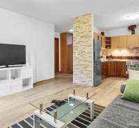 Living room in a two-room apartment, wooden decor flooring, kitchen, TV, sofa.