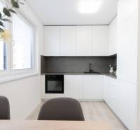 A kitchen in a 2-room apartment with white cabinets, a gray countertop, and a large window.