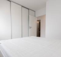 Bedroom in a 2-room apartment with a sliding wardrobe and a white bed.