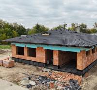 A family house under construction in Bernolákovo, surrounded by greenery and building materials.