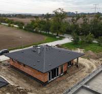 A family house in Bernolákovo with a black roof and surrounding fields under construction.