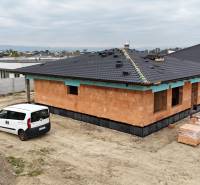A family house under construction in Bernolákovo, a car in the foreground, neighboring buildings.