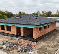 A family house in Bernolákovo under construction, surrounding trees, gray roof.
