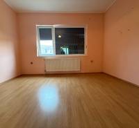 A room in a family house with a wooden decor floor and pink walls.
