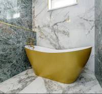 Golden bathtub with marble walls in the bathroom of a family house.