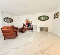 The interior of a family house with a white floor and brown furniture, decorative paintings on the walls.