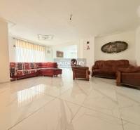 A bright living room in a family house with tiles, a red sofa, and brown armchairs.