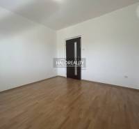An empty room in a 3-room apartment with a wood-patterned floor and dark doors.