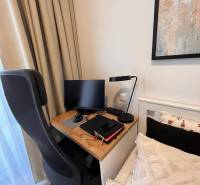 A workspace in a studio apartment with a computer, chair, and lamp next to the bed.