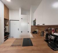 The interior of a kitchen in a one-room apartment with wooden decor and white cabinets.