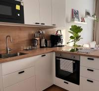 A kitchen in a studio apartment with white cabinets and a wood-patterned floor.