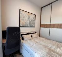A bed with a desk, chair, and painting in a studio apartment with a wardrobe.