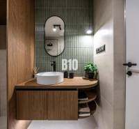 A bathroom with green tiles, an oval mirror, and a wooden-patterned floor.