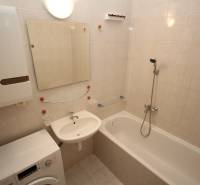 Bathroom in a studio apartment with a bathtub, washing machine, and sink on light tiles.