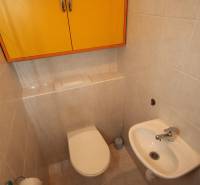 A toilet in a one-room apartment with a chrome holder and a yellow cabinet on the wall.