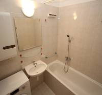 Bathroom in a studio apartment with a bathtub, sink, and washing machine, bright tiles.