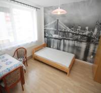 A room with a bed, a table, and a photo wallpaper of a bridge in a studio apartment, with a floor featuring a wooden decor.