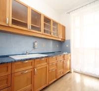A kitchen in a studio apartment with wooden cabinets and a floor with a wood decor.