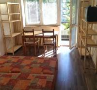 A one-room apartment with a wooden decor floor, a bed, a table, chairs, and shelves.