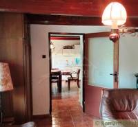 Interior of a cabin with a comfortable armchair, lamp, and a view into the kitchen.