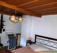 The interior of a cabin with a wooden ceiling, a bed, a small table, and ceramic lamps.