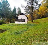 A cottage in Chocholná-Velčice surrounded by greenery and forest on a mowed meadow.