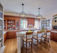 A kitchen in a villa with a wood-patterned floor, wooden cabinets, and an island with stools.