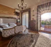 A bedroom in a villa with a bed, a wall mural of palm trees, and a wooden decor floor.