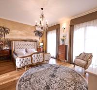 Luxury bedroom with an upholstered bed, palm wallpaper, and wood-patterned flooring.