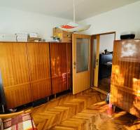 A room with furniture, wood-patterned flooring, and a television in a three-room apartment.