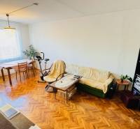 Living room with wood-patterned flooring in a 3-room apartment, includes a couch and a table.