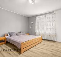 A bedroom in a family house with a bed, a wooden decor floor, and light curtains.