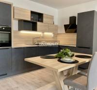 A kitchen in a 3-room apartment with a wood-patterned floor, black cabinets, and wooden accessories.