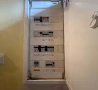 An open electrical panel in a family house with attached labels and white walls.